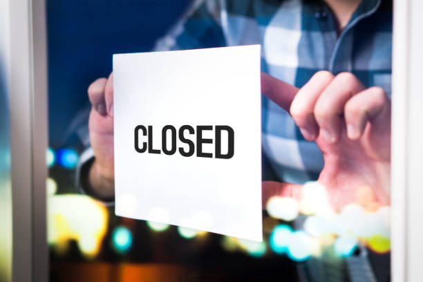 Bankruptcy, failed business going down or opening times concept. Man putting closed sign in window in cafe, restaurant, shop, store or agency.