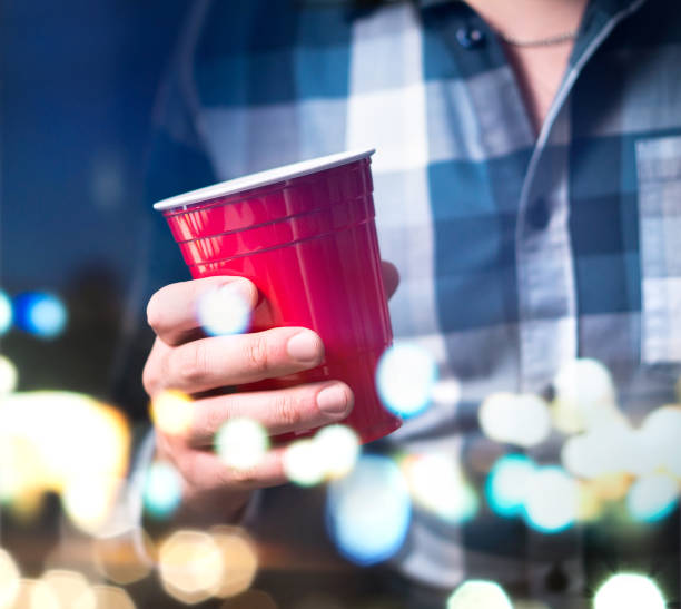 Young man holding red cup in a luxury party. Person having fun and drinking alcohol. Young man holding red cup in a luxury party. Person having fun and drinking alcohol. Abstract and modern celebration concept. red party cup stock pictures, royalty-free photos & images