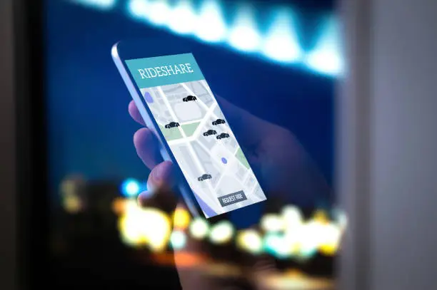 Ride sharing and carpool mobile application. Rideshare taxi app on smartphone screen. Modern online people and commuter transportation service. Man holding phone late at night. City street lights.