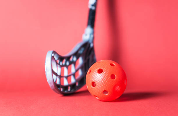 Floorball stick and ball against red background. Floor hockey concept.