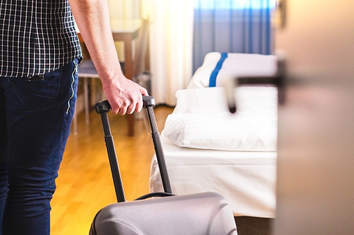 Man pulling suitcase and entering hotel room. Traveler going in to room or walking inside motel with luggage. Travel and holiday apartment rental concept.