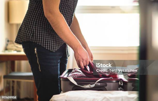 Maleta De Embalaje En Habitación De Hotel Hombre Joven De Camiseta Plegable En El Equipaje En Casa Habitación Equipaje Libre En Cama Para La Preparación De Vacaciones Foto de stock y más banco de imágenes de Empaquetar