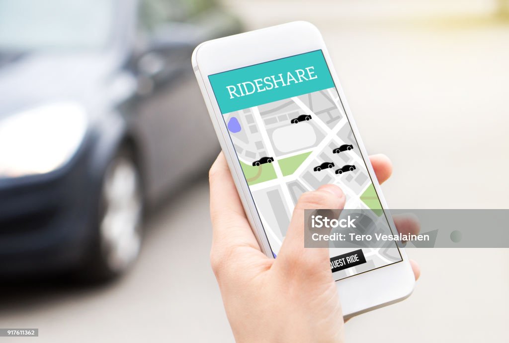 Ride share taxi service on smartphone screen. Online rideshare app and carpool mobile application. Woman holding phone with a car in the background. Ride share taxi service on smartphone screen. Online rideshare app and carpool mobile application. Woman holding phone with a car in the background. Person ordering ride with cellphone. Car Pooling Stock Photo