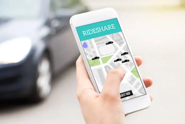 Ride share taxi service on smartphone screen. Online rideshare app and carpool mobile application. Woman holding phone with a car in the background. Person ordering ride with cellphone.