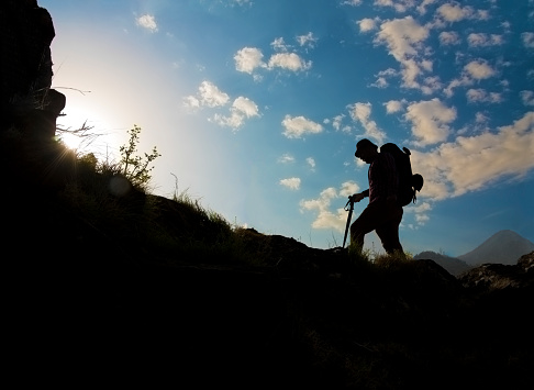 Silhouette of a man hiking in Himalayan mountains with the backpack. Extreme mountainous terrain. Outdoors on a cloudy day blue sky.