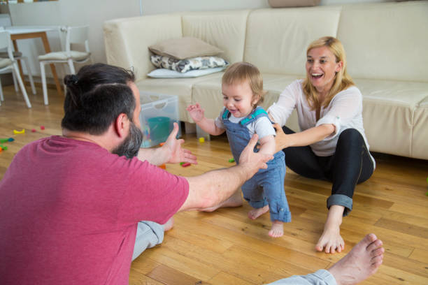 glückliche eltern helfen kleinen sohn zu fuß im wohnzimmer - furniture barefoot little boys family stock-fotos und bilder