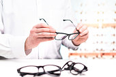 Optician in store holding glasses. Eye doctor with lenses. Professional optometrist in white coat with many eyeglasses. Shop interior.