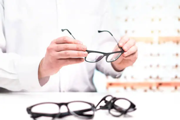 Photo of Optician in store holding glasses. Eye doctor with lenses. Professional optometrist in white coat with many eyeglasses. Shop interior.