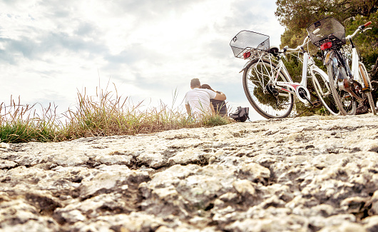 Couple on a bike trip. Lovers sitting on beach, rock, cliff by the sea or forest in nature. Bicycles parked for taking break from cycling. Man and woman on a romantic date or picnic.