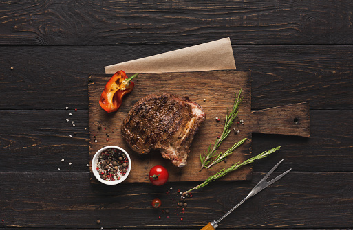 Grilled meat and vegetables on rustic wooden table. Fried steak on bone, restaurant serving with spices and herbs, top view