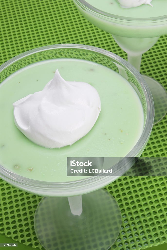 Green pistachio pudding with whipped cream in a margarita glass Green colored pistachio  pudding with a dollop of whipped cream on top. It is being served in a frosted margarita glass. There is a partial view of a second glass of pudding. The background is a different hue of green for color consistency and contrast. Shot in the studio under natural light.  Cold Temperature Stock Photo