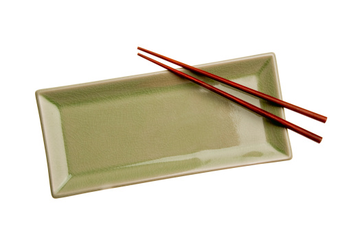 A green rectangular Asian style plate with brown wooden chopsticks, sits on a white background.