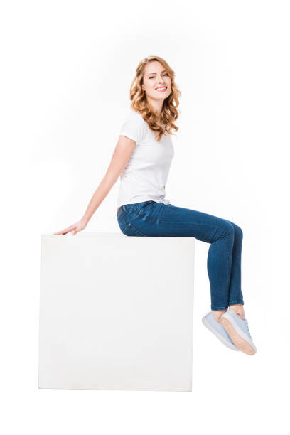 istock cheerful woman sitting on empty  white cube isolated on white 917626074