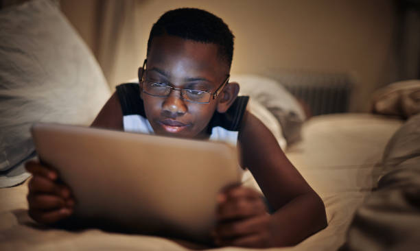 Wireless tech keeping him wide awake Shot of a young boy using a digital tablet at night in bed reading glasses stock pictures, royalty-free photos & images