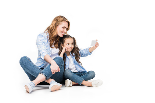 happy mother and daughter taking selfie on smartphone together isolated on white