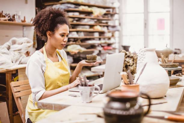 istock Woman Holding Pottery Craft, Looking at Laptop 917641264
