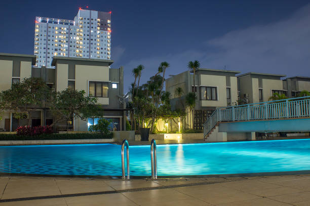 istock Pool at night with lush greenery and lighting for home design and landscaping in the backyard.  Night shadows and reflections on the pool water. 917641356