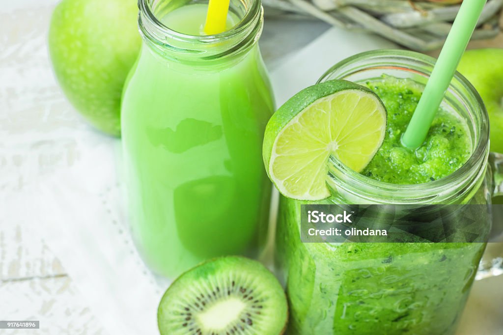 Glass Mason Jar and Bottle with Green Vegetable and Fruit Smoothie and Juice with Straw. Basket with Seasonal Organic Produce in Background. Spring Summer Detox Glass Mason Jar and Bottle with Green Vegetable and Fruit Smoothie and Juice with Straw. Basket with Seasonal Organic Produce in Background. Spring Summer Detox Healthy Diet. Juice - Drink Stock Photo