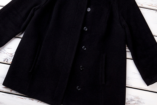 Female black buttoned coat. New collection of female outwear, wooden background. Female elegance and style.