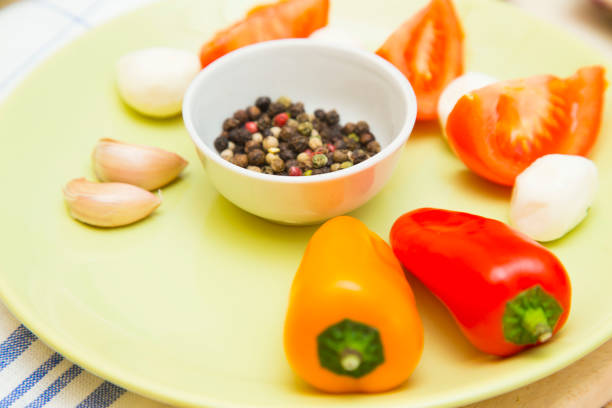 Set of raw ingredients for Italian salad on a plate and tablecloth background. Garlic, salad, tomatos, red and yellow papper. Set of healthy food products. Closeup