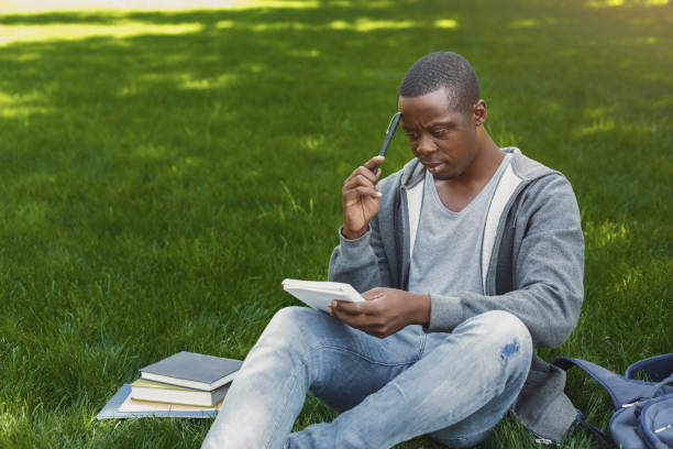 istock Concentrated african-american studen sitting with notebook on grass 917660166
