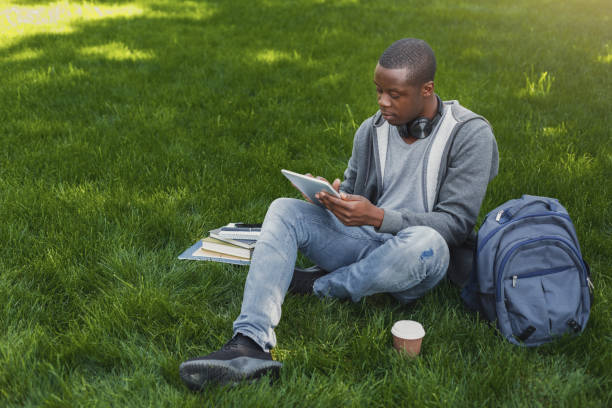 istock African-american student on grass with tablet oudoors 917660368