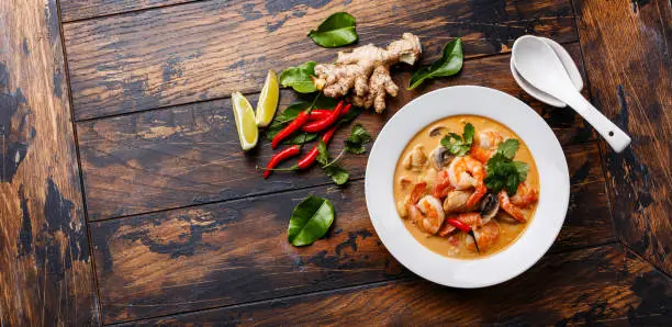 Tom Yam kung Spicy Thai soup with shrimp, seafood, coconut milk and chili pepper in bowl on wooden background copy space