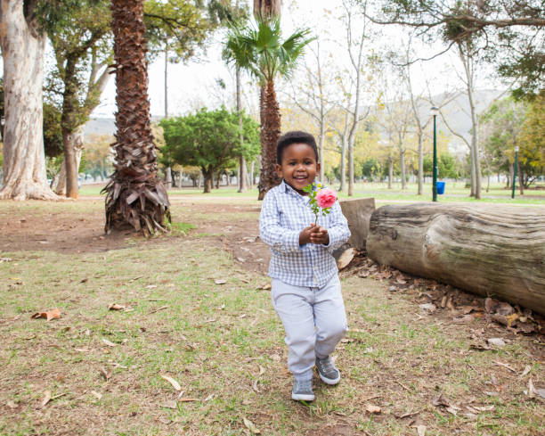 African child walking with a rose in his hand, the rose is pink and the boy is smiling.
