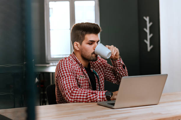 istock Confident young man working on laptop and drinking coffee while sitting at his working place in office. 917677128