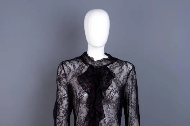 Female frill collar black lace blouse. Feminine elegant transparent blouse with jabot on mannequin, grey background.