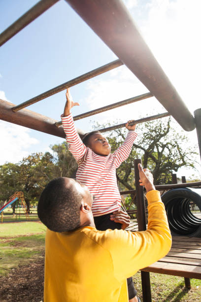 Father lifts his child to reach monkey bars on a jungle gym. stock photo