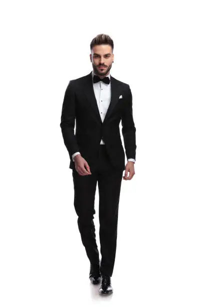 happy young male fashion model in tuxedo is walking on white background