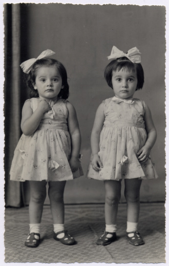 Hi-res scan of an italian photograph dated 1957. Two little twin sisters are looking at camera with identical frocks, hair bows and shoes.