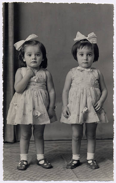 Vintage photo - little twin sisters Hi-res scan of an italian photograph dated 1957. Two little twin sisters are looking at camera with identical frocks, hair bows and shoes. twin photos stock pictures, royalty-free photos & images