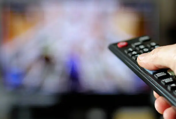 Hand with remote control and TV in the background