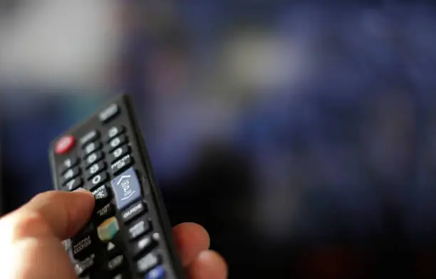 Hand with remote control and blurred TV in the background