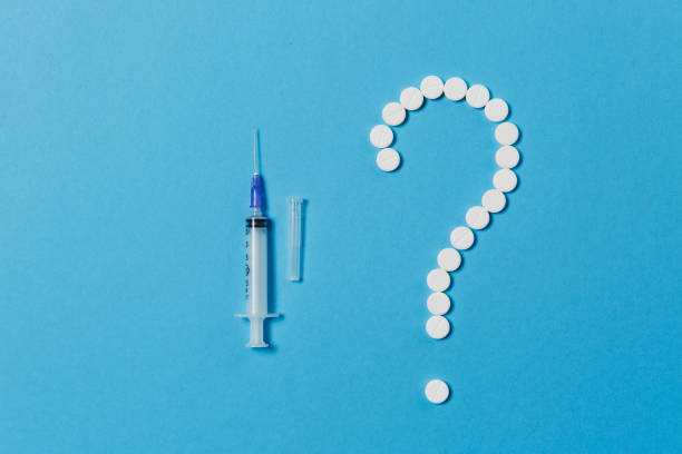 istock Medication white round tablets arranged in question mark shape isolated on blue color background. Pills, empty syringe with needle, sign. Concept of health, treatment, choice, healthy lifestyle. 917710694
