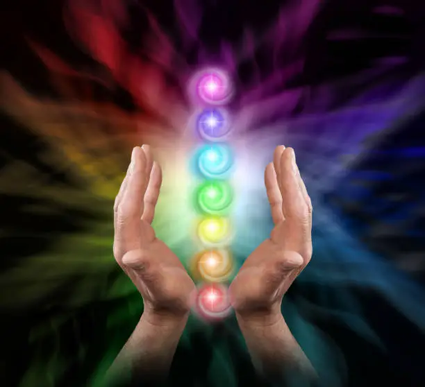 Male parallel hands facing upwards against a multicoloured background of energy and the Seven Chakras floating between his hands