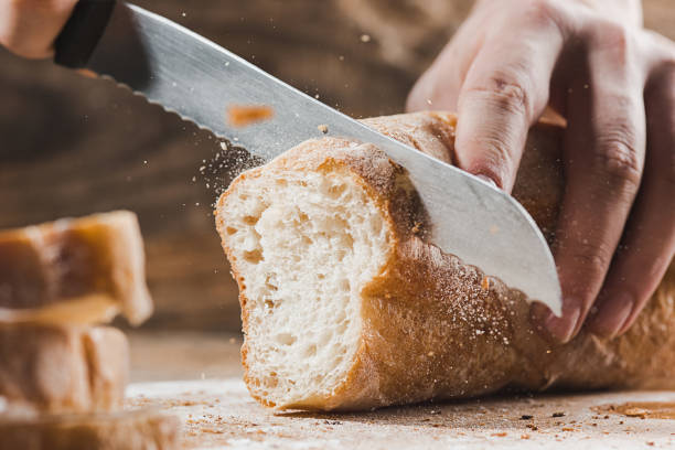 pain de grains entiers mis sur planche de bois de cuisine avec un chef tenant or couteau pour couper - cooks knife photos et images de collection