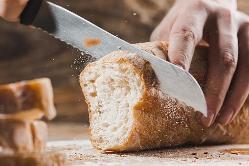 Whole grain bread put on kitchen wood plate with a chef holding gold knife for cut. Fresh bread on table close-up. Fresh bread on the kitchen table The healthy eating and traditional bakery concept. Rustic style