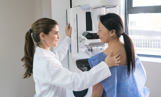 Female gynecologist helping a patinet get in posicion for a mammogram both looking happy and smiling