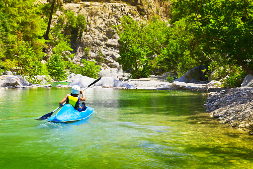 Young unidentified sportsman kayaking along mountain river in sunny summer day