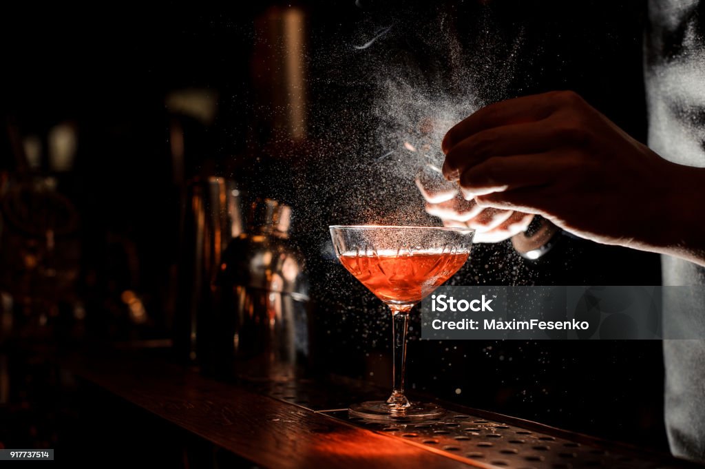 Barmans hands sprinkling the juice into the cocktail glass Barmans hands sprinkling the juice into the cocktail glass filled with alcoholic drink on the dark background Cocktail Stock Photo