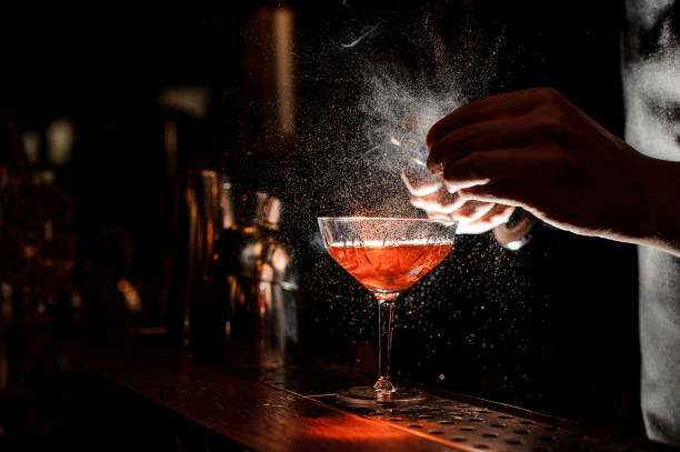 Barmans hands sprinkling the juice into the cocktail glass Barmans hands sprinkling the juice into the cocktail glass filled with alcoholic drink on the dark background whiskey photos stock pictures, royalty-free photos & images
