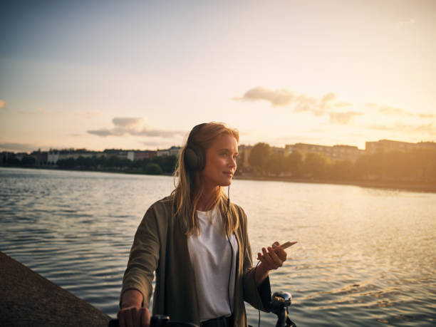 Music and this scenery is all she needs Cropped shot of a beautiful young woman listening to music with her cellphone outside lake scandinavia stock pictures, royalty-free photos & images