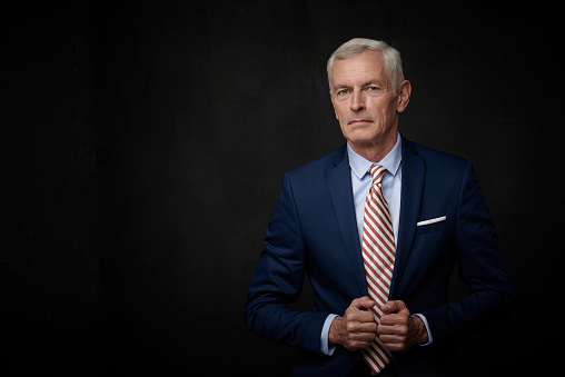 Executive senior lawyer businessman wearing suit and looking at camera while standing at isolated black background with copy space.