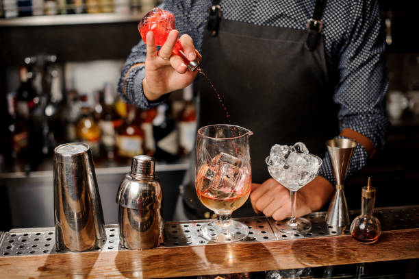 istock Bartender pouring red sweet fruit syrup into the large cocktail glass 917755238
