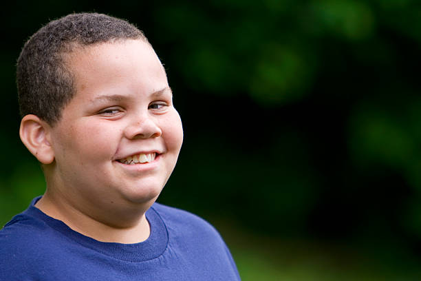 A happy boy with close cropped hair and a blue shirt grins Happy latino boy with a cheesy grin overweight boy stock pictures, royalty-free photos & images