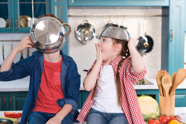 istock adorable little children having fun with utensils while sitting on kitchen table 917758868