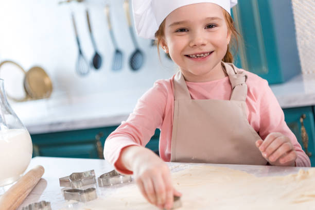 istock adorable child in chef hat and apron smiling at camera while preparing cookies 917759204